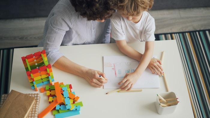 A parent and child drawing and working together at a table at home.