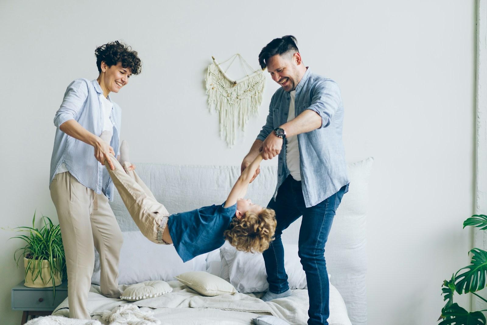Two parents playfully swinging their young child between them in a bright room.